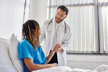 Afro-Amerikan hasta hastasını hastane koğuşunda teselli eden neşeli Hintli doktor.