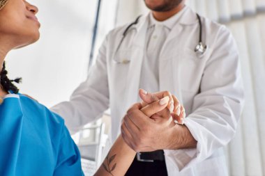 Afro-Amerikan hastasını hastanenin koğuşunda rahatlatan neşeli Hintli doktor görüntüsü.