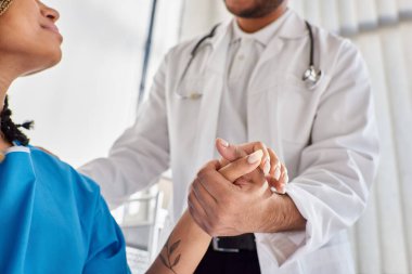 cropped view of jolly indian doctor comforting his african american patient in her hospital ward clipart