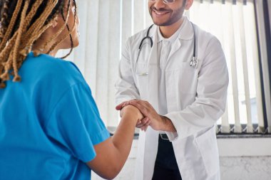 cropped view of jolly indian doctor shaking hands with his cheerful african american patient clipart