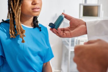Genç Hintli doktor hasta Afrikalı Amerikalı kadın hastasına astım spreyini nasıl kullanacağını öğretiyor.