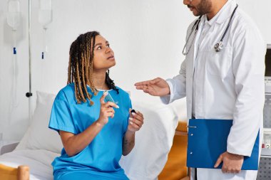 Genç Hintli doktor, hasta Afrikalı Amerikalı kadın hastasına astım spreyini nasıl kullanacağını öğretiyor.