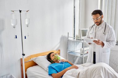 Genç Hintli doktor, hasta Afrikalı Amerikalı kadın hastasına oksijen maskeli, sağlık hizmetlerinde yardım ediyor.