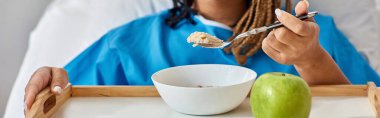 cropped view of young ill african american woman having her breakfast in hospital bed, banner clipart