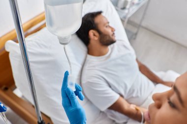 focus on african american nurse setting drop counter next to her blurred indian male patient clipart