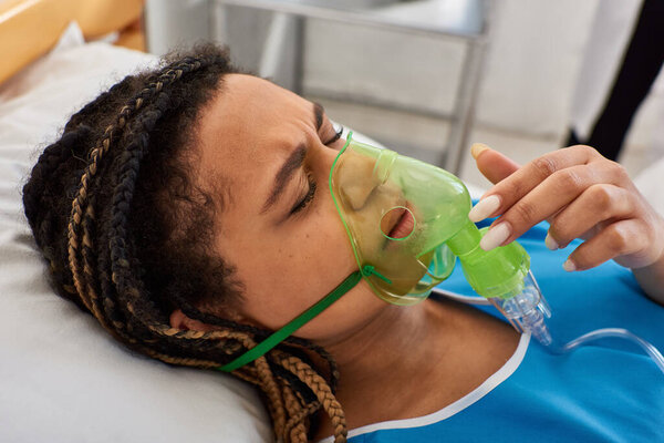 ill young african american woman lying in hospital bed in her ward with oxygen mask, healthcare
