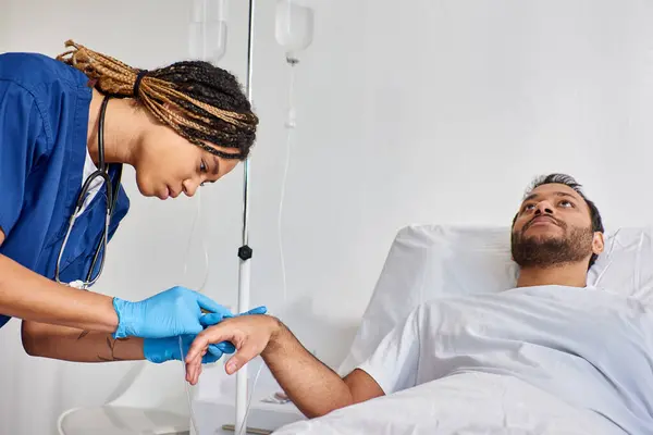 stock image young african american nurse inserting catheter into arm of her sick indian patient, healthcare