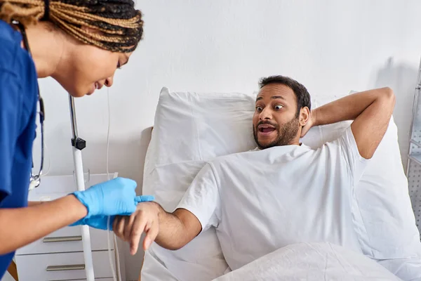 stock image young african american nurse inserting catheter into arm of her sick indian patient, healthcare