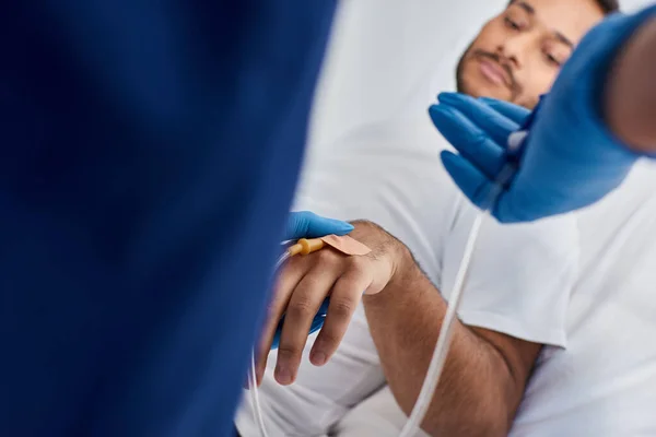 Stock image cropped view of african american nurse inserting catheter into arm of her indian patient, healthcare