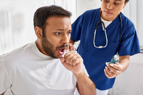 young african american nurse giving asthma inhaler to her ill indian patient in his ward, healthcare