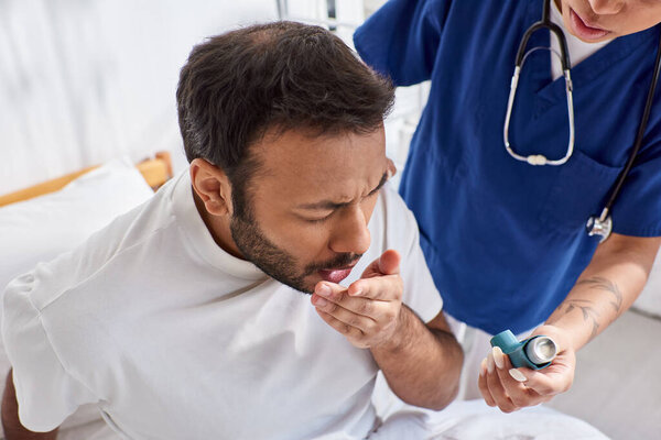 young african american nurse giving asthma inhaler to her ill indian patient in his ward, healthcare