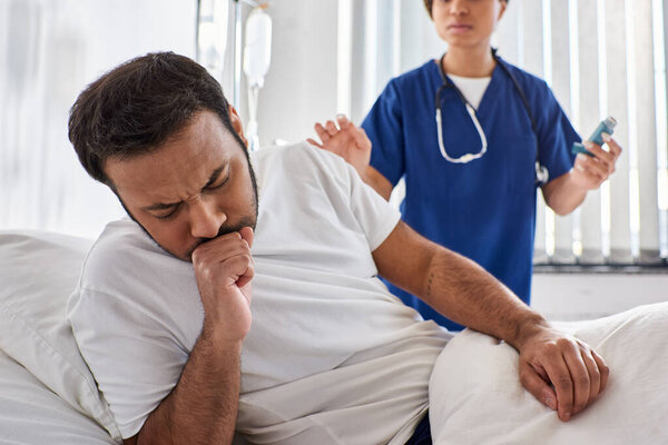 young african american nurse giving asthma inhaler to her ill indian patient in his ward, healthcare