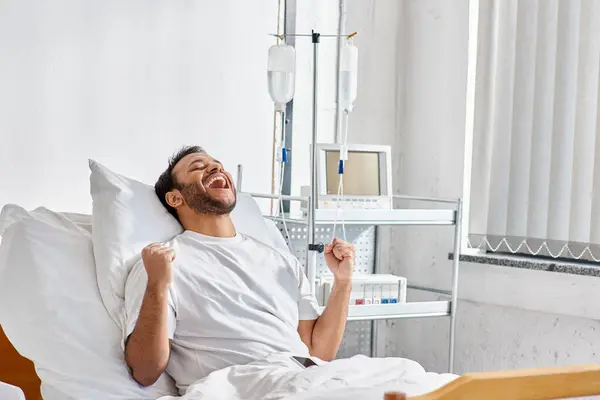 young happy indian patient cheering and gesturing actively while in hospital bed, healthcare
