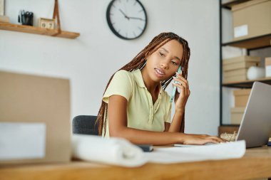 Çekici Afrikalı Amerikalı kadın tüccar paketleri üzerinde çalışırken telefonla konuşuyor.
