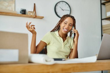 Neşeli, çekici Afro-Amerikan kadın satıcı paketleri üzerinde çalışırken telefonla konuşuyor.