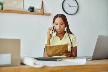 Çekici Afrikalı Amerikalı kadın satıcı telefonla konuşuyor ve posta paketine bakıyor.