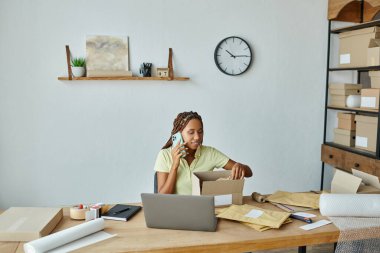 Çekici Afrikalı Amerikalı kadın satıcı telefonla konuşuyor ve karton kutu paketliyor.