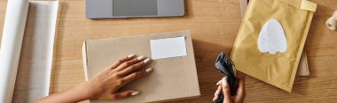 cropped view of african american woman holding scanner next to box while working hard, delivery clipart