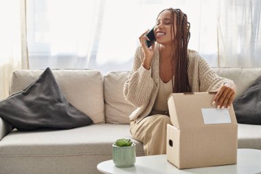 Neşeli, çekici, Afro-Amerikan kadın rahat bir ev elbisesi içinde telefonla konuşuyor.