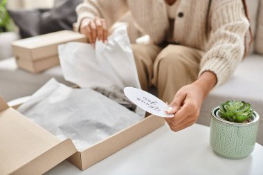 Afro-Amerikalı genç bir kadının elinde paketleri açarken çıkardığı teşekkür çıkartması.