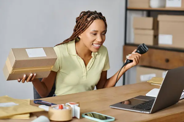 stock image cheerful african american female merchant looking at laptop while scanning box, delivery concept