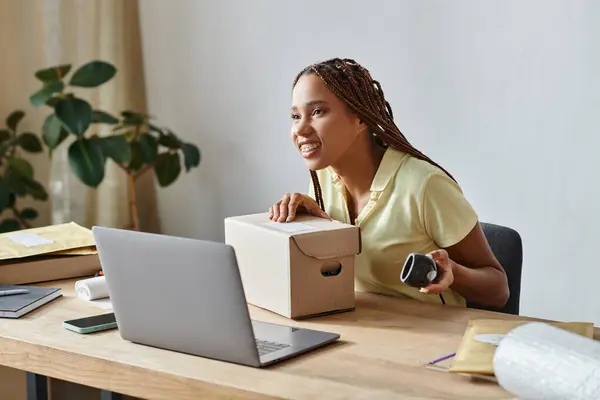 joyous african american female seller with braces holding scanner next to box, delivery concept