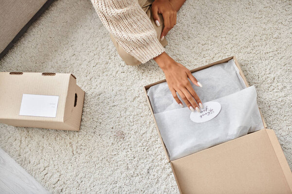 обрезанный вид на молодую африканскую американскую женщину распаковывает свою новую посылку с благодарственной наклейкой на ней