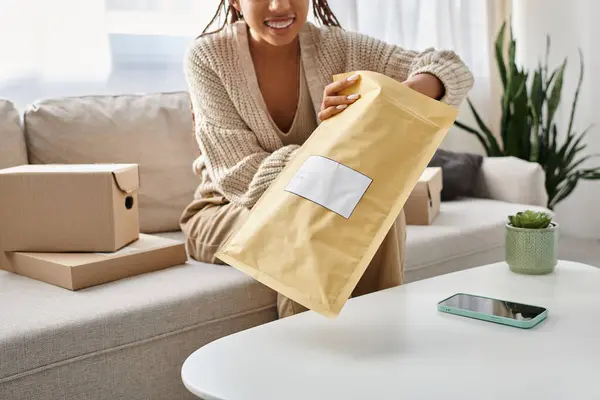 cropped view of young jolly african american woman with braces opening post packet at home