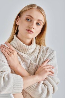 Beyaz, sıcak süveter giyen sarışın kadın gri kış atmosferinde otururken kameraya bakıyor.