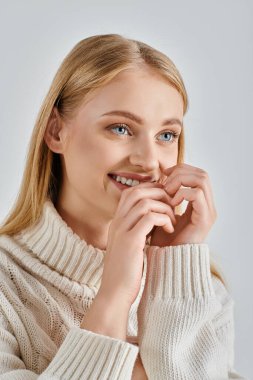 Beyaz, sıcak süveter ve doğal makyajla gülümseyen, yüzü griye yakın genç, neşeli kadın.