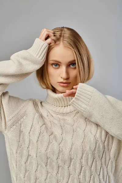 stock image young woman with blonde hair and expressive gaze posing in white knitted sweater on grey backdrop