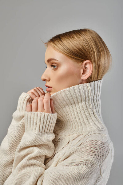 profile portrait of blonde woman in white knitted sweater with high collar on grey, winter style
