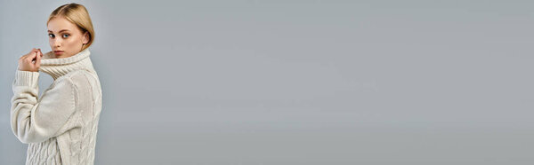 blonde woman in knitted sweater with high collar looking at camera on grey, banner with copy space