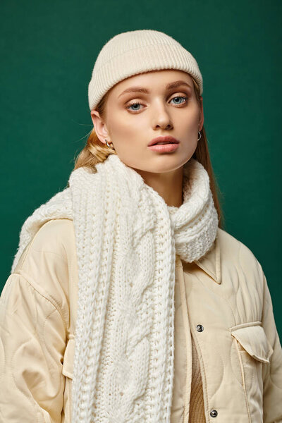 trendy woman in warm jacket and knitted scarf with beanie hat on green backdrop, winter fashion