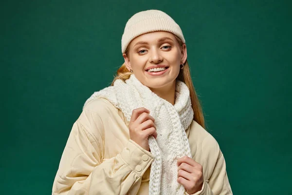 stock image happy woman in warm jacket and knitted scarf with beanie hat on green backdrop, winter casual trend