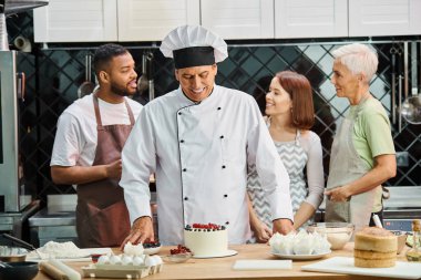 joyous chef in white hat looking at his delicious cake next to his diverse students, cooking courses clipart