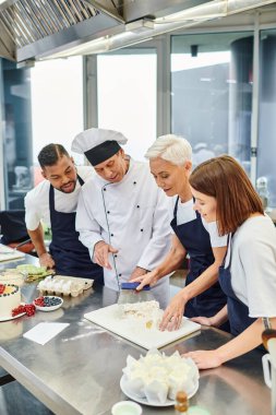 İyi görünümlü, çok kültürlü, mavi önlüklü, hamurla çalışan çok kültürlü pastacılar.