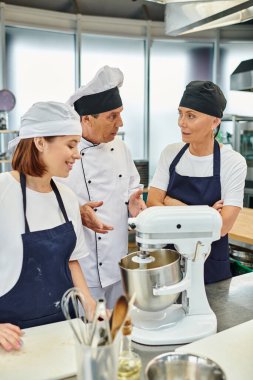 Şef aşçının yanında gülümseyen neşeli genç kadın ve meslektaşı bir şey tartışıyorlar, şekerleme.