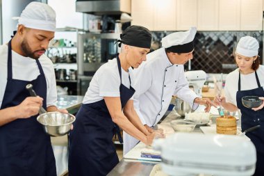 handsome mature chief cook talking to his young chef while others working hard, confectionery clipart