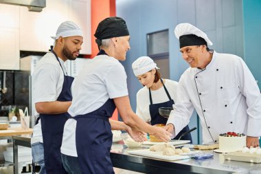 Mutlu olgun aşçı ve şef gülümserken ırklar arası meslektaşları pasta üzerinde çalışıyor.