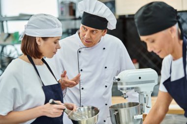 focus on mature chief cook listening to his young chef next to her mature colleague, confectionery clipart