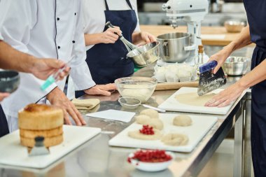 cropped view of hard working chefs and chief cook working with dough on kitchen, confectionery clipart