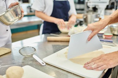 Genç iş arkadaşı ve aşçısının yanında hamur kesen olgun bir kadın manzarası.