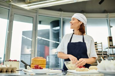 Mavi önlüklü neşeli, genç, çekici şef hamurla çalışıyor ve başka tarafa bakıyor, şekerlemeler.