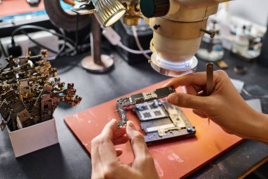Elektronik cihazın tamiratı sırasında çip setini tutan teknisyenlerin kırpılmış görünümü
