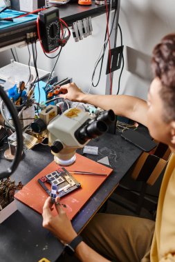 Bulanık adam, atölyede profesyonel ekipman yakınında mikro elektronik cihaz montajı yapıyor