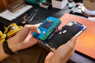 Modern atölyede voltmetre ve akıllı telefonlu tamirci görüntüsü.