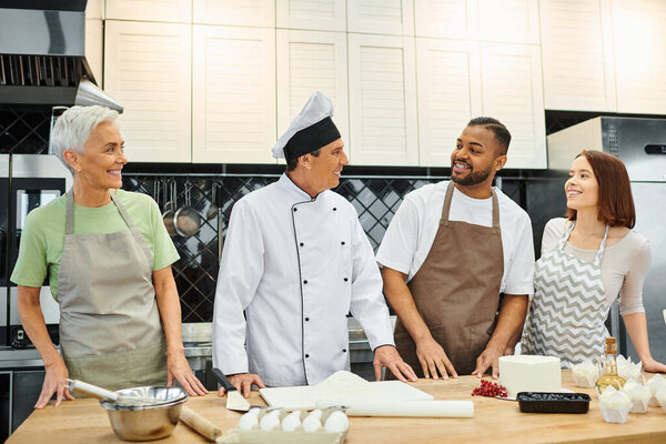 cheerful chef looking at his diverse students while teaching them how to bake, cooking courses