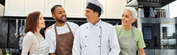 jolly diverse students smiling at mature joyous chef during cooking lesson, confectionery, banner