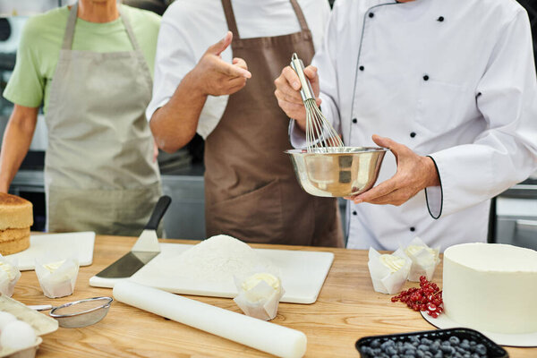 cropped view of mature chef whisking dough in front of his multicultural students, cooking courses